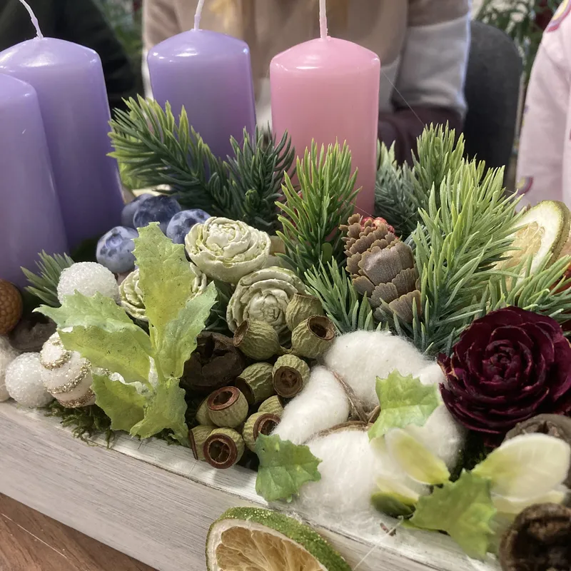 Adventi koszorú lila és rózsaszín gyertyákkal, fenyőágakkal, termésekkel és szárított citrusszelettel